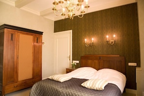 Une chambre à coucher avec une grande armoire en bois, un lit recouvert d’une courtepointe matelassée et un lustre.