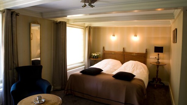 Una habitación de hotel con cama, una silla, una mesa y un espejo.