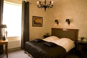 Une chambre à coucher avec un grand lit, un lustre, un tableau et une fenêtre avec des rideaux.