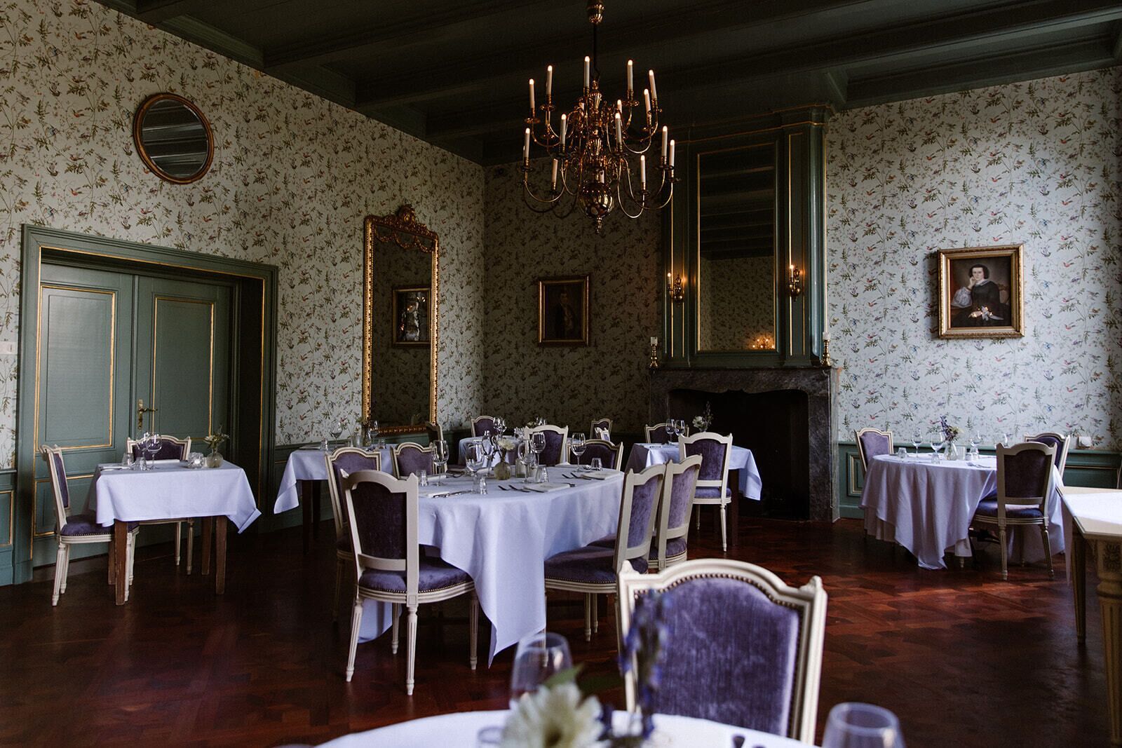 Comedor con varias mesas dispuestas para una comida, un candelabro y una chimenea.