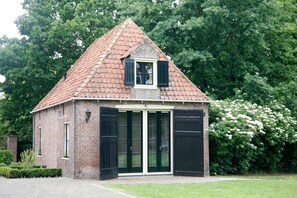 Un pequeño edificio de ladrillo con techo inclinado, puertas de cristal grandes y una ventana pequeña con contraventanas.