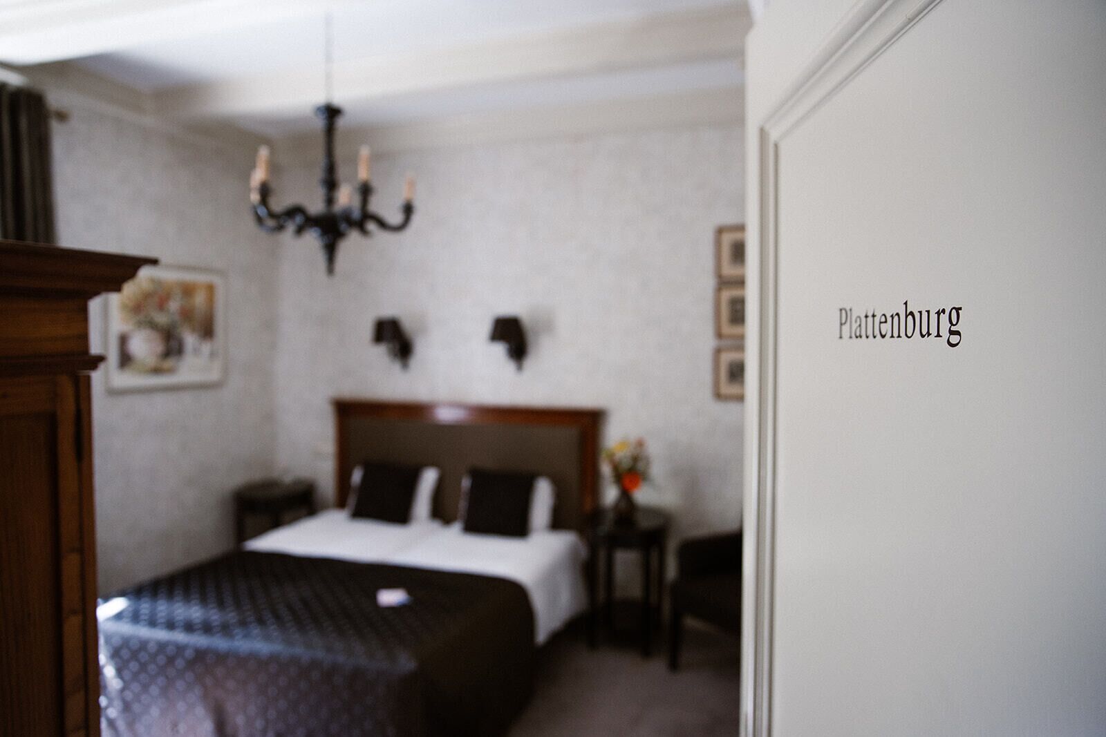 Quarto de hotel com cama, mesa de cabeceira, abajur e lustre.