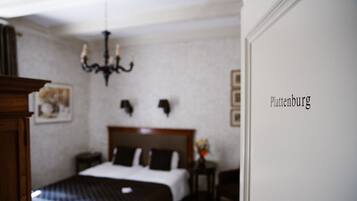 Quarto de hotel com cama, mesa de cabeceira, abajur e lustre.
