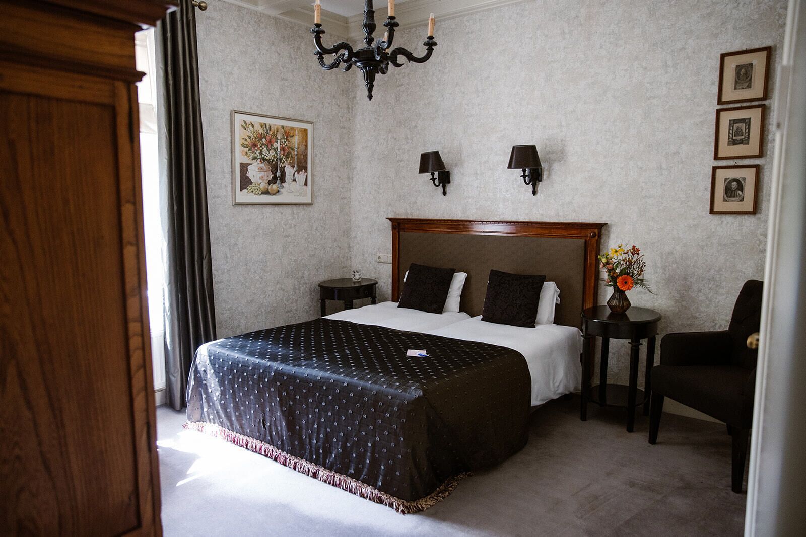 Habitación de hotel con una cama grande, cabecera de madera, una mesita con un florero y una silla.