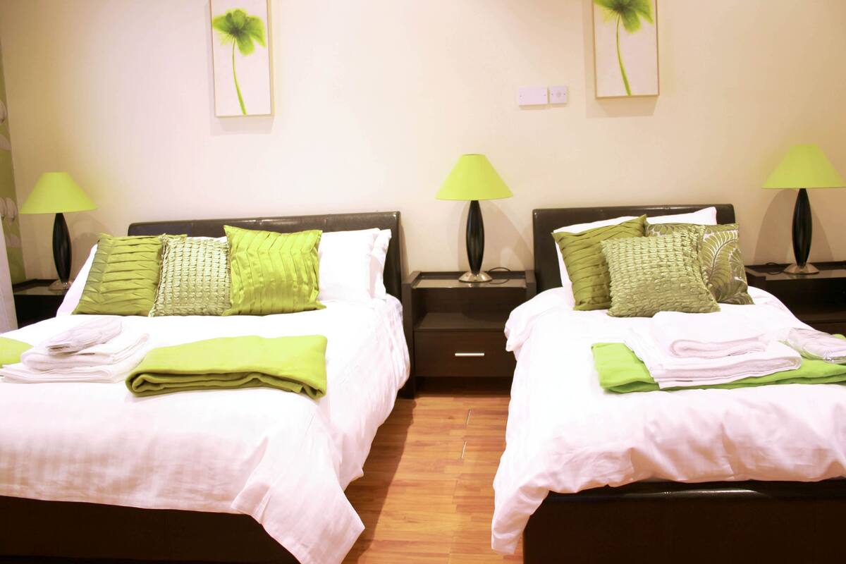 Two twin beds with green and white bedding, nightstands with lamps, and a wooden floor.