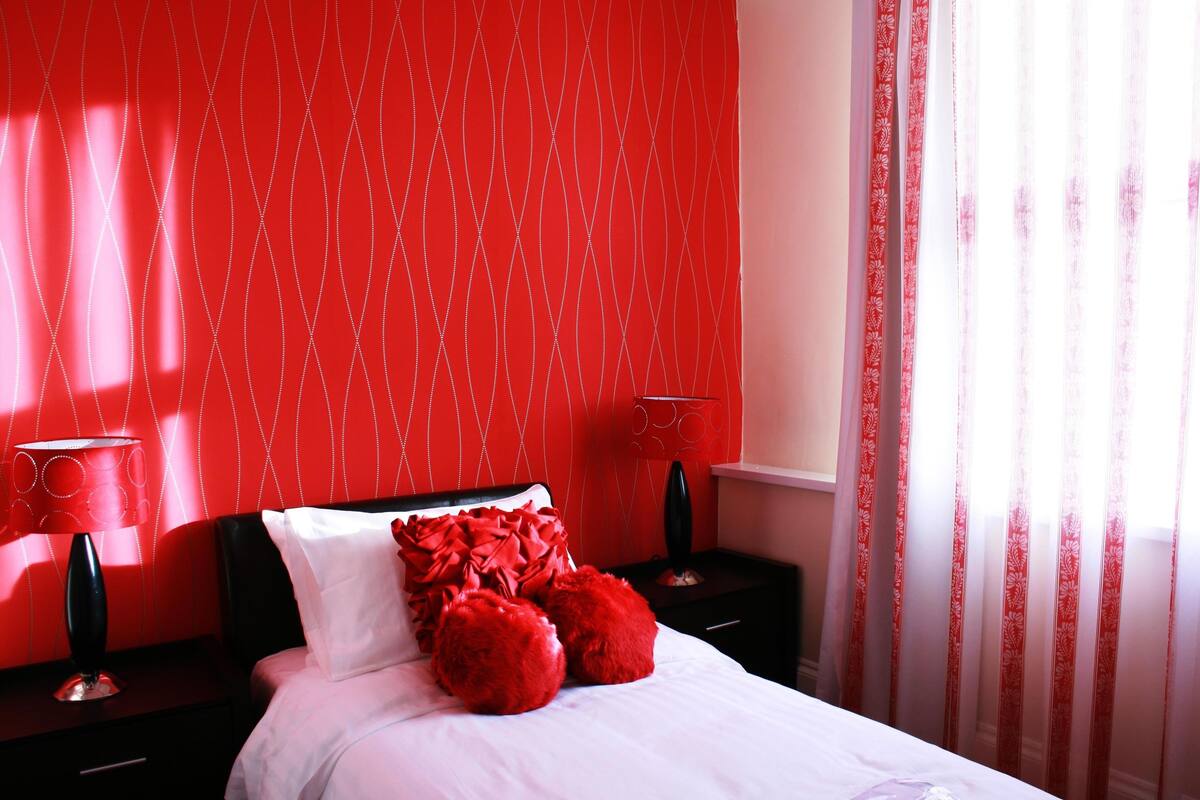 A red-themed bedroom with a bed, pillows, and bedside tables.