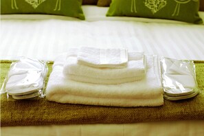 A neatly folded stack of white towels on a green towel on a bed with white sheets and green pillows. - Hotel Makedonia (London)