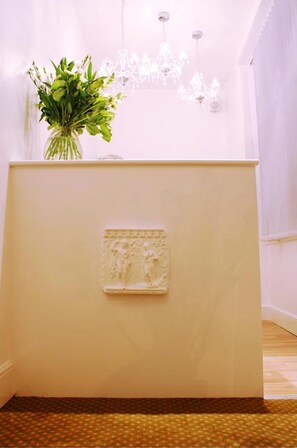 A reception desk with a vase of flowers, a chandelier, and a wall-mounted sculpture. - Hotel Makedonia (London)