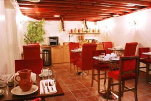A dining area with red chairs, a wooden table, and a kitchen in the background. - Hotel Makedonia (London)