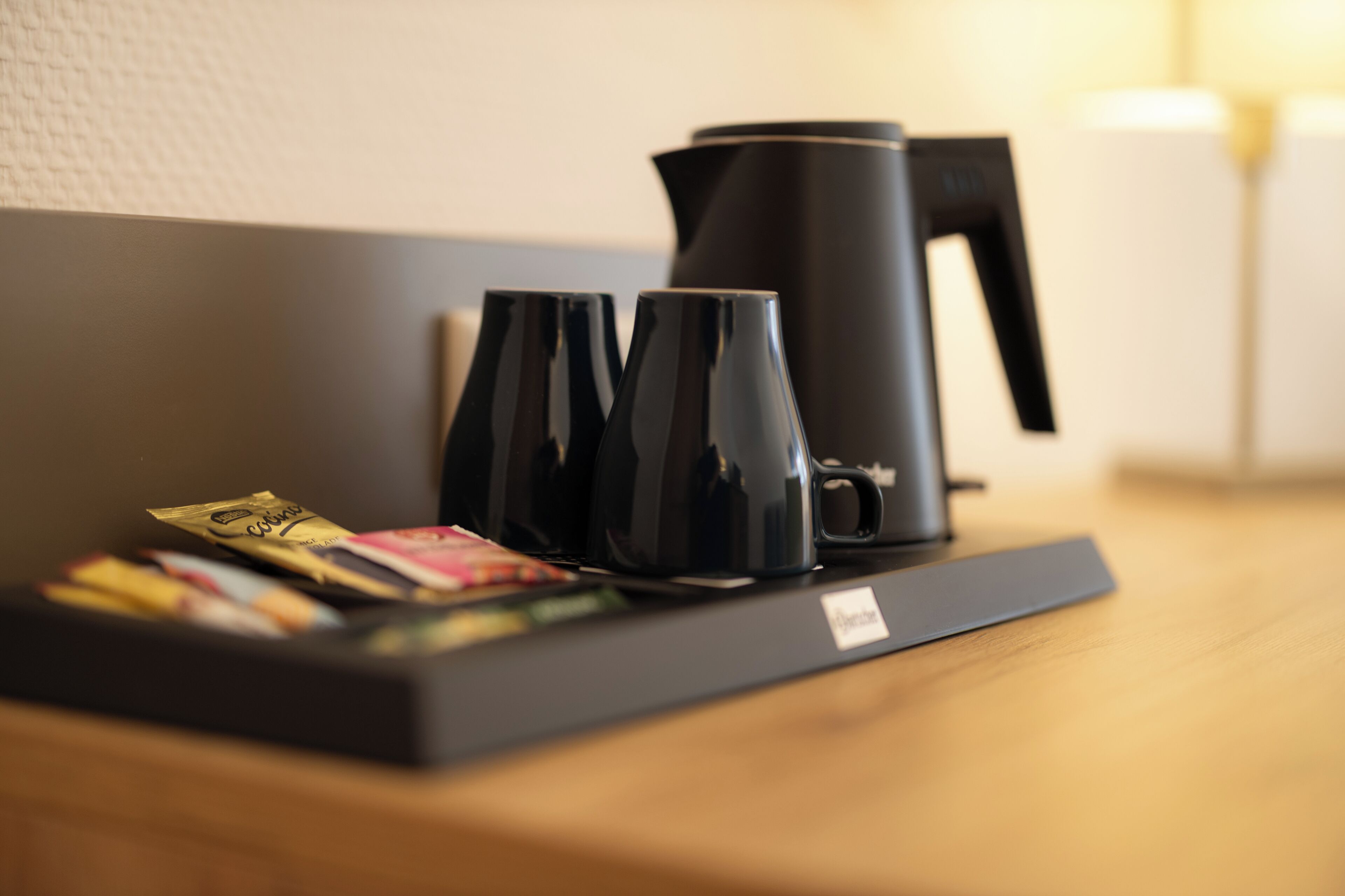 A coffee maker, two cups, and a tray with coffee pods on a wooden table.