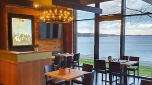 Um restaurante com área de bar, grandes janelas com vista para a água e piso de madeira.