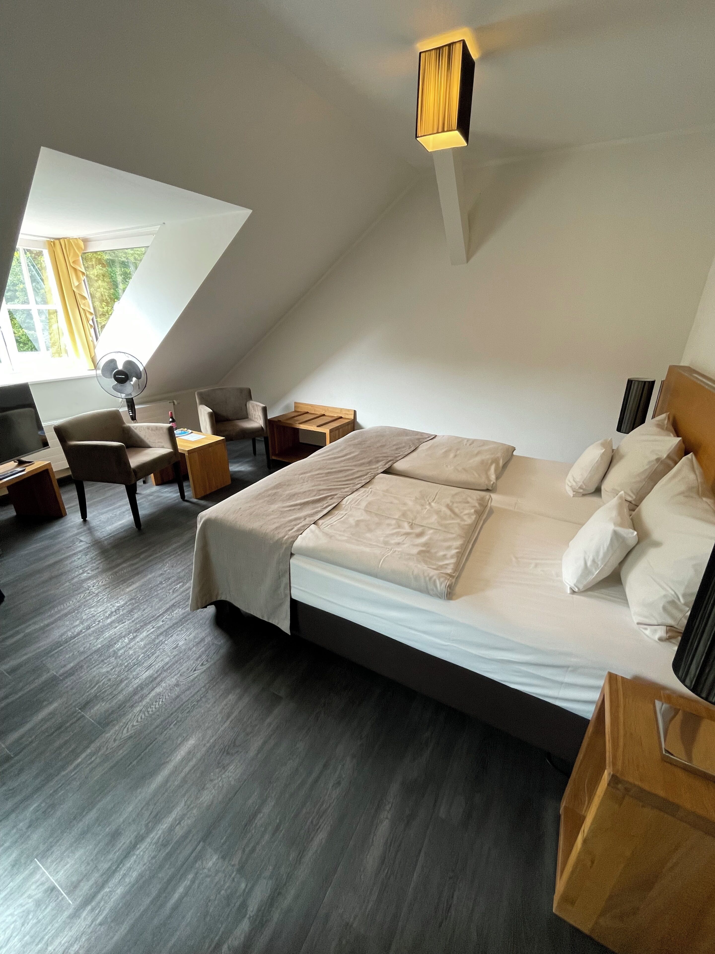 Ein modernes Schlafzimmer mit einem großen Bett, einem Schreibtisch, einem Stuhl und einem Standventilator.