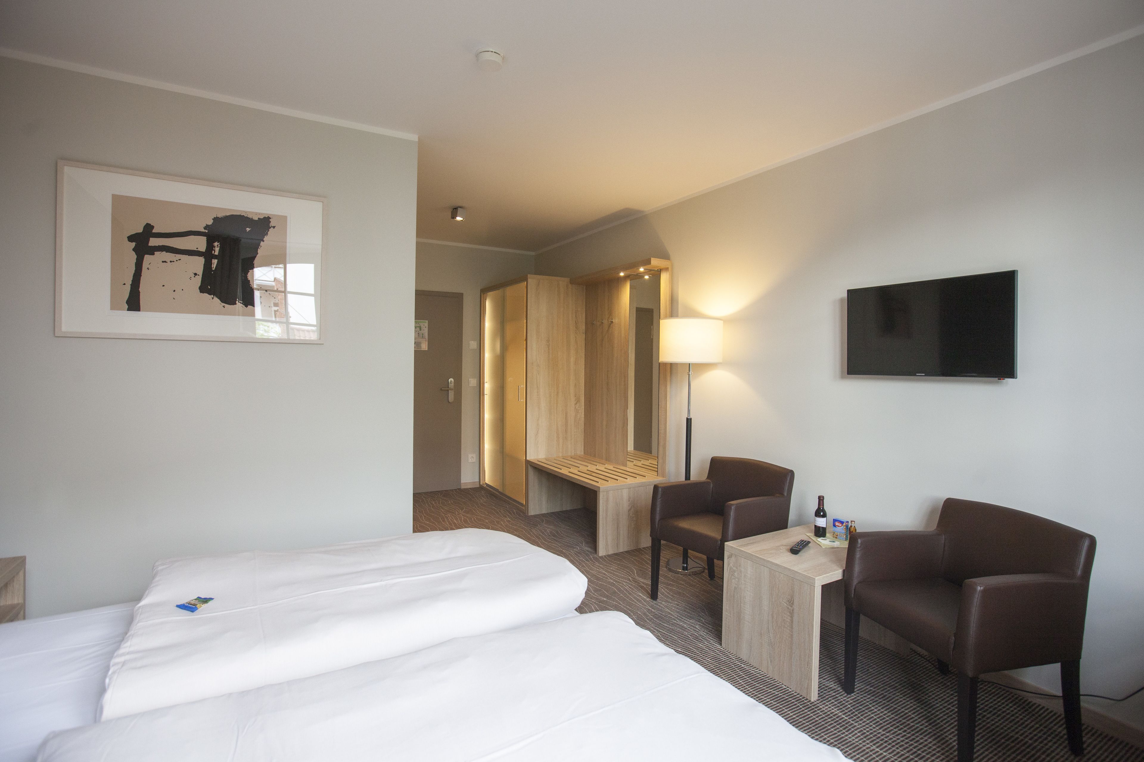 Habitación de hotel con dos camas, un escritorio, una silla, un televisor y un cuadro en la pared.
