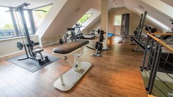 A gym with various exercise equipment, a bench, and a large window providing natural light.