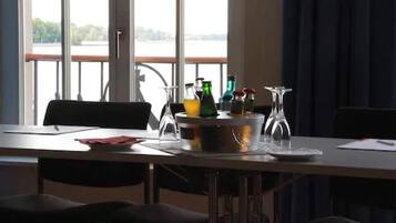 En matplats med ett bord dukat för två personer, ett fönster med utsikt över en sjö eller ett annat vattendrag och en balkong med ett räcke.