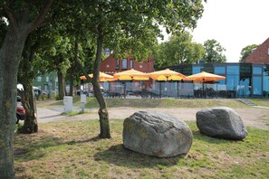 Un parque con rocas grandes, árboles y asientos exteriores con sombrillas amarillas.