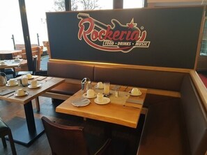 Un interior de restaurante con mesas dispuestas para comer, el logotipo de Rockeria y un tablero de menú.