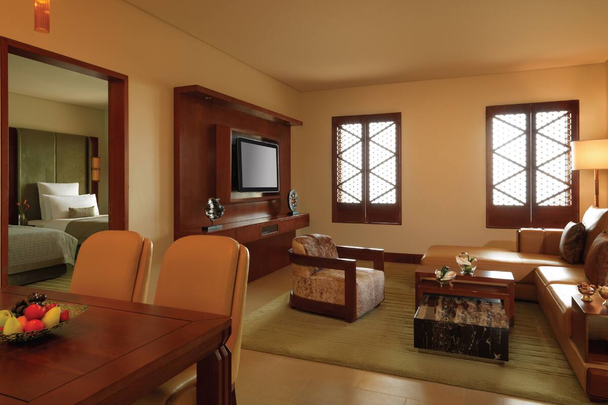 Habitación de hotel con comedor, sofá, televisor y ventanas amplias.