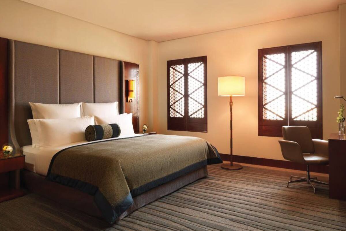 Habitación de hotel con una cama grande, un escritorio, una silla y dos ventanas con paneles decorativos.