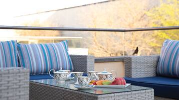A balcony with wicker furniture, striped cushions, and a table with teapots and fruit.