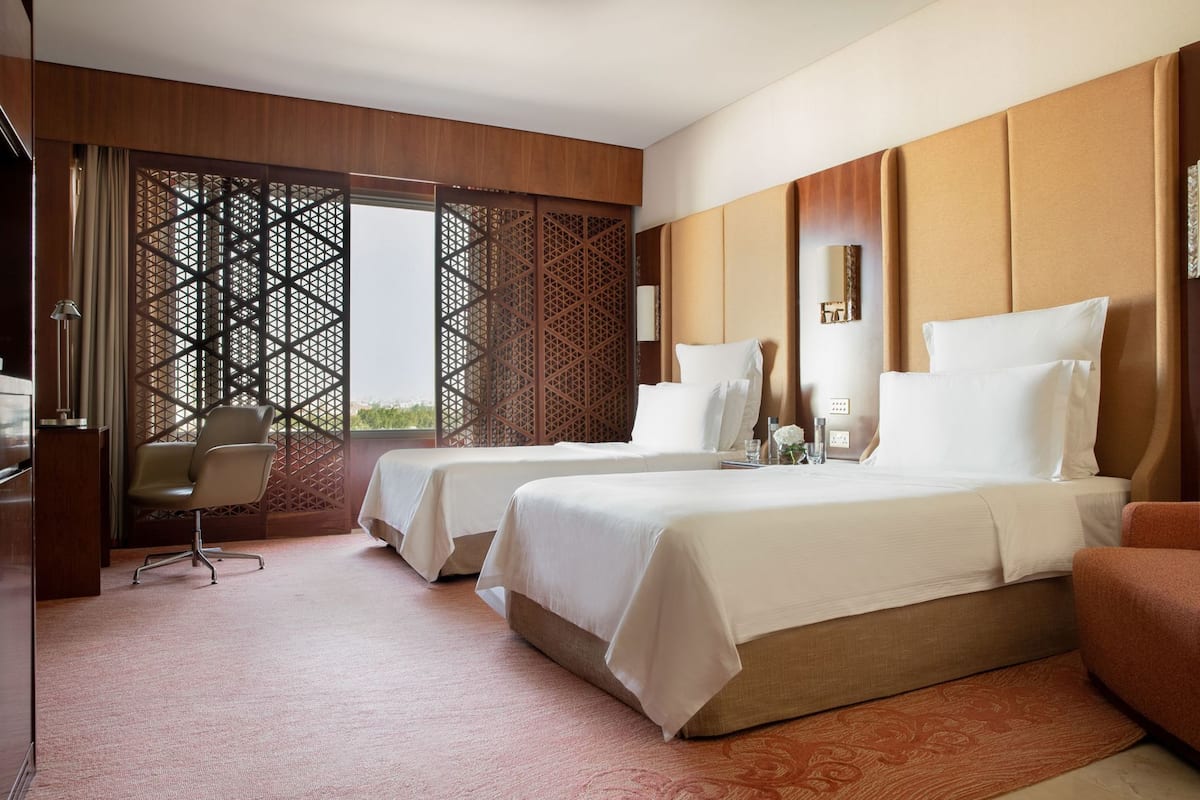 A hotel room with two beds, a desk, a chair, and a decorative screen.