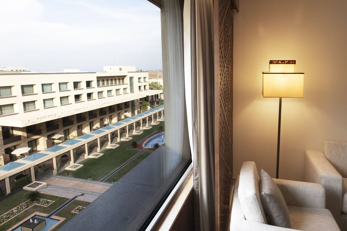 A hotel room with a view of a courtyard, a lamp, and a chair.