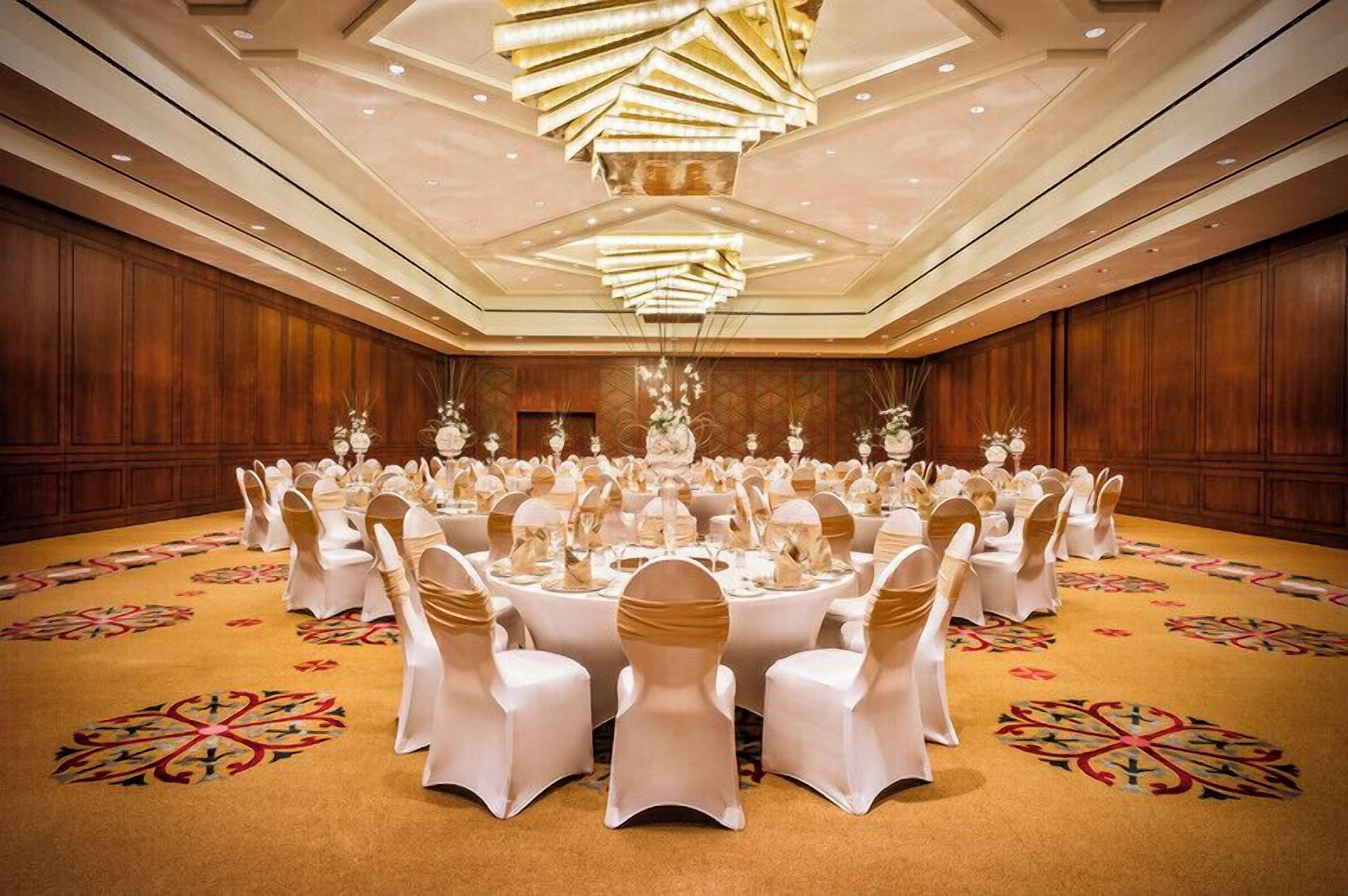 A large banquet hall with round tables, white tablecloths, and gold sashes.