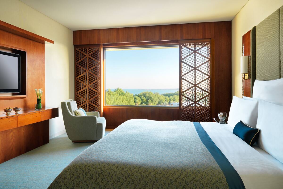A hotel room with a large bed, a TV, a chair, and a view of the outdoors.