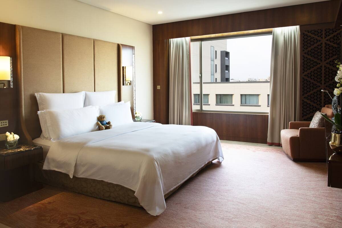 A hotel room with a large bed, a nightstand, a chair, and a window with curtains.