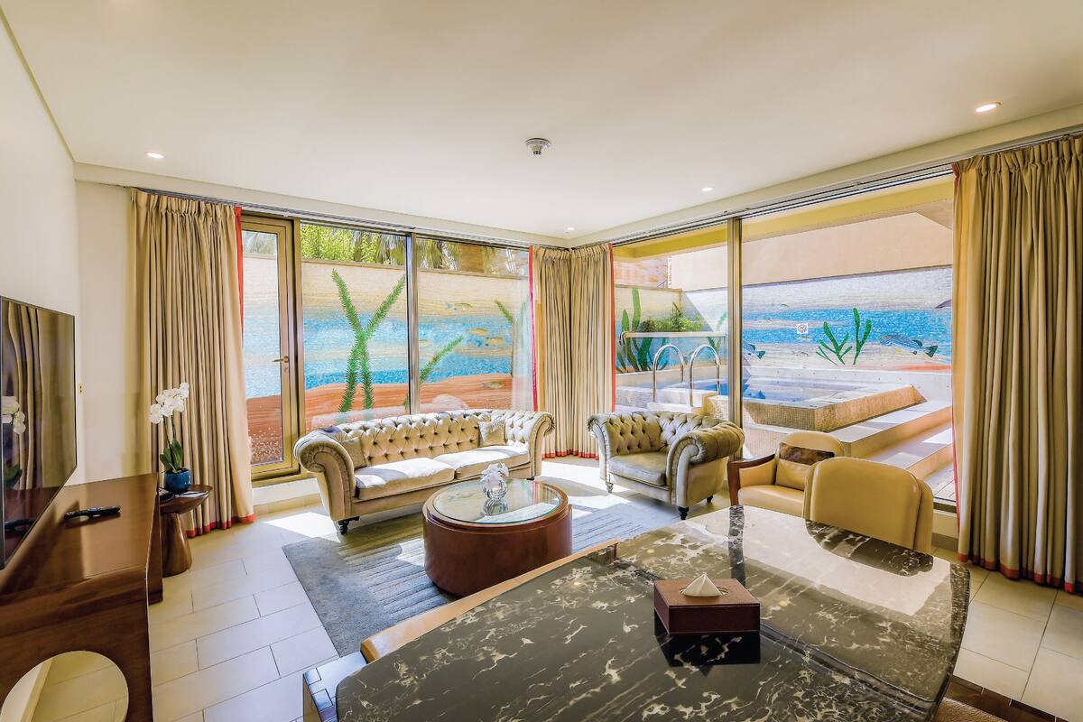 Amplio salón con grandes puertas de vidrio que dan a una zona de piscina, amoblado con sofás y una mesa de centro.
