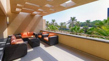 A balcony with outdoor furniture, a view of palm trees, and a modern architectural design.