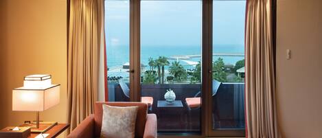 Habitación de hotel con sofá, una mesa con lámpara y vistas al mar a través de amplios ventanales.
