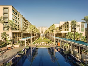 Un hôtel doté d’une piscine centrale, de palmiers et d’une architecture symétrique.