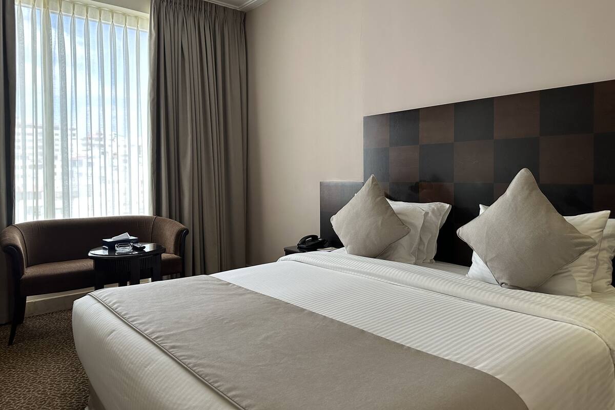 Habitación de hotel con una cama grande, una silla, una mesita pequeña y una mesita de noche con un teléfono.