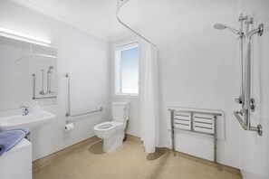 A modern bathroom with a toilet, sink, shower, and a window with blinds. - Oakleigh Motel (Gore)