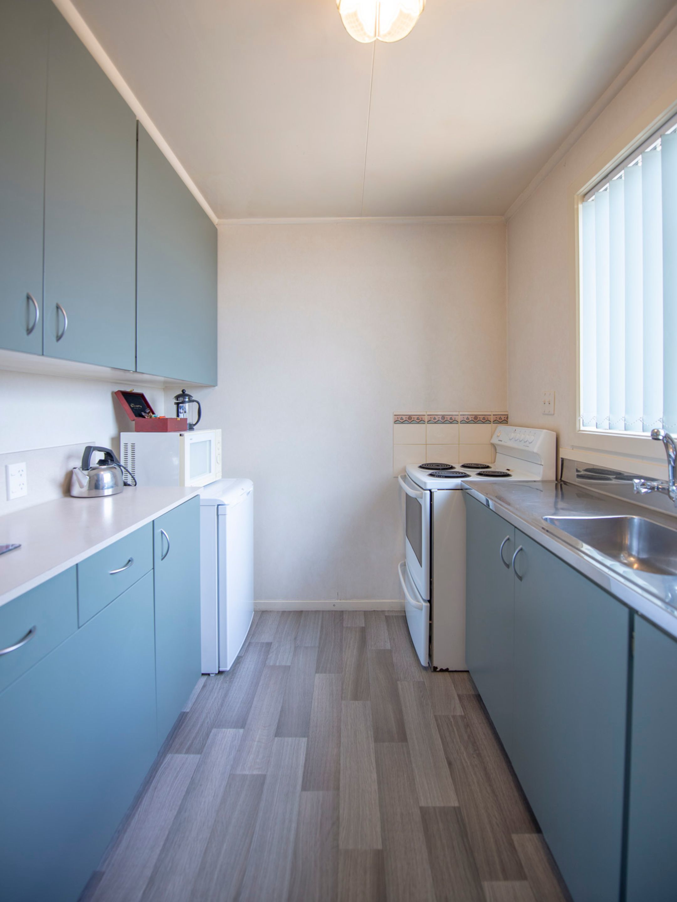 Una cocina compacta con armarios azul claro, un refrigerador blanco, una estufa y un ventanal que proporciona luz natural.
