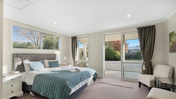 Quarto moderno com uma cama grande, mesa de cabeceira, cadeira e vista para o exterior através de uma porta de vidro deslizante.