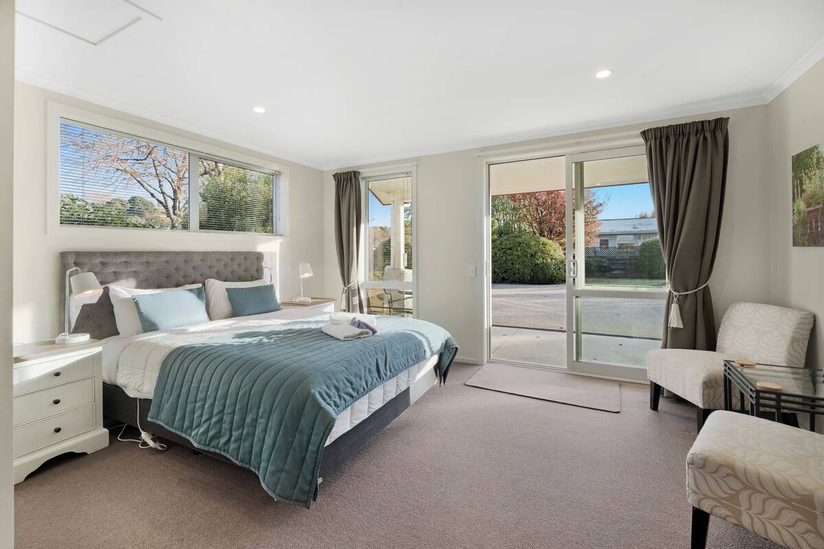 A modern bedroom with a large bed, a bedside table, a chair, and a view of the outdoors through a sliding glass door.