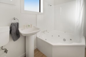 A bathroom with a white sink, a bathtub, and a window above the sink. - Oakleigh Motel (Gore)