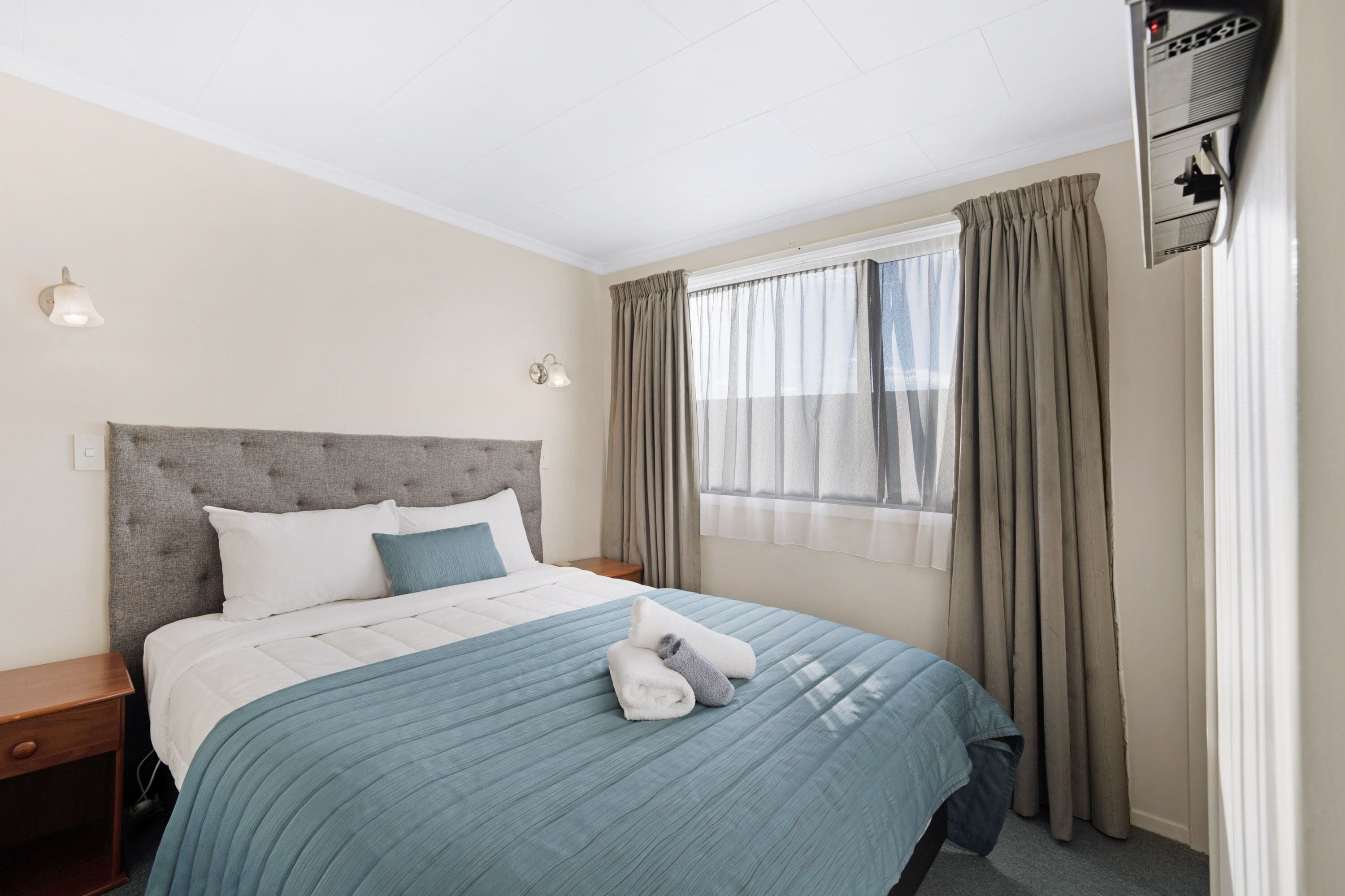 Une chambre d’hôtel comprenant un lit, une table de chevet, une fenêtre avec des rideaux et un climatiseur fixé au mur.