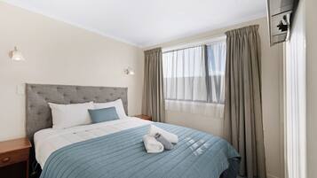 Une chambre d’hôtel comprenant un lit, une table de chevet, une fenêtre avec des rideaux et un climatiseur fixé au mur.