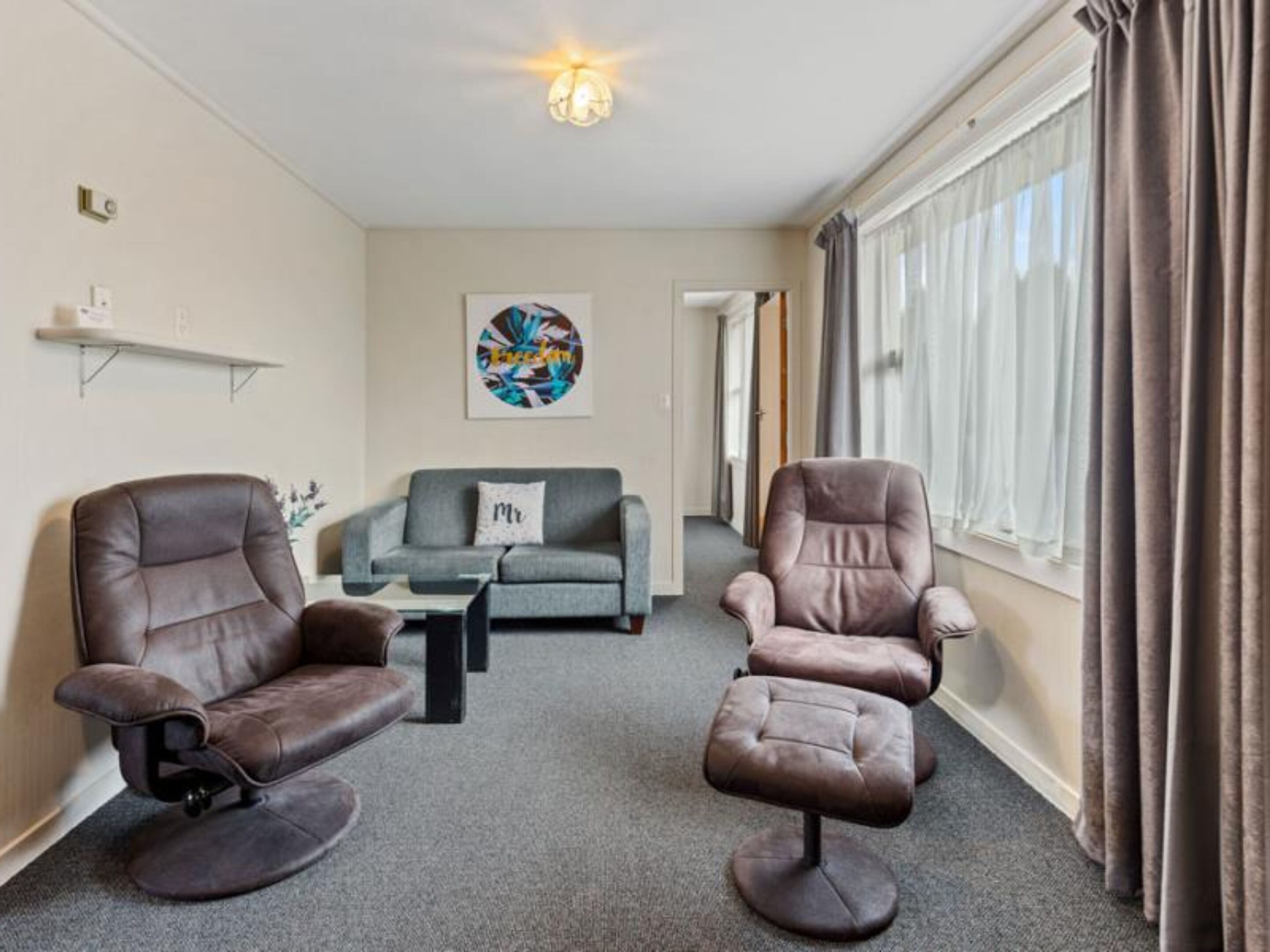 A living room with two leather chairs, a grey sofa, a coffee table, and a painting on the wall.