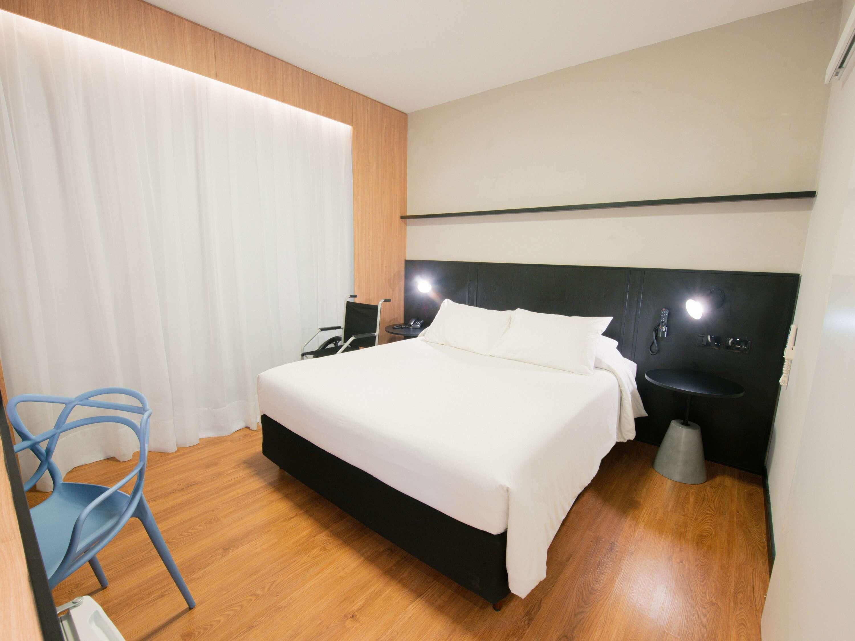 Moderni hotellihuone, jossa on suuri sänky, yöpöytä, tuoli ja pieni kylpyhuone.