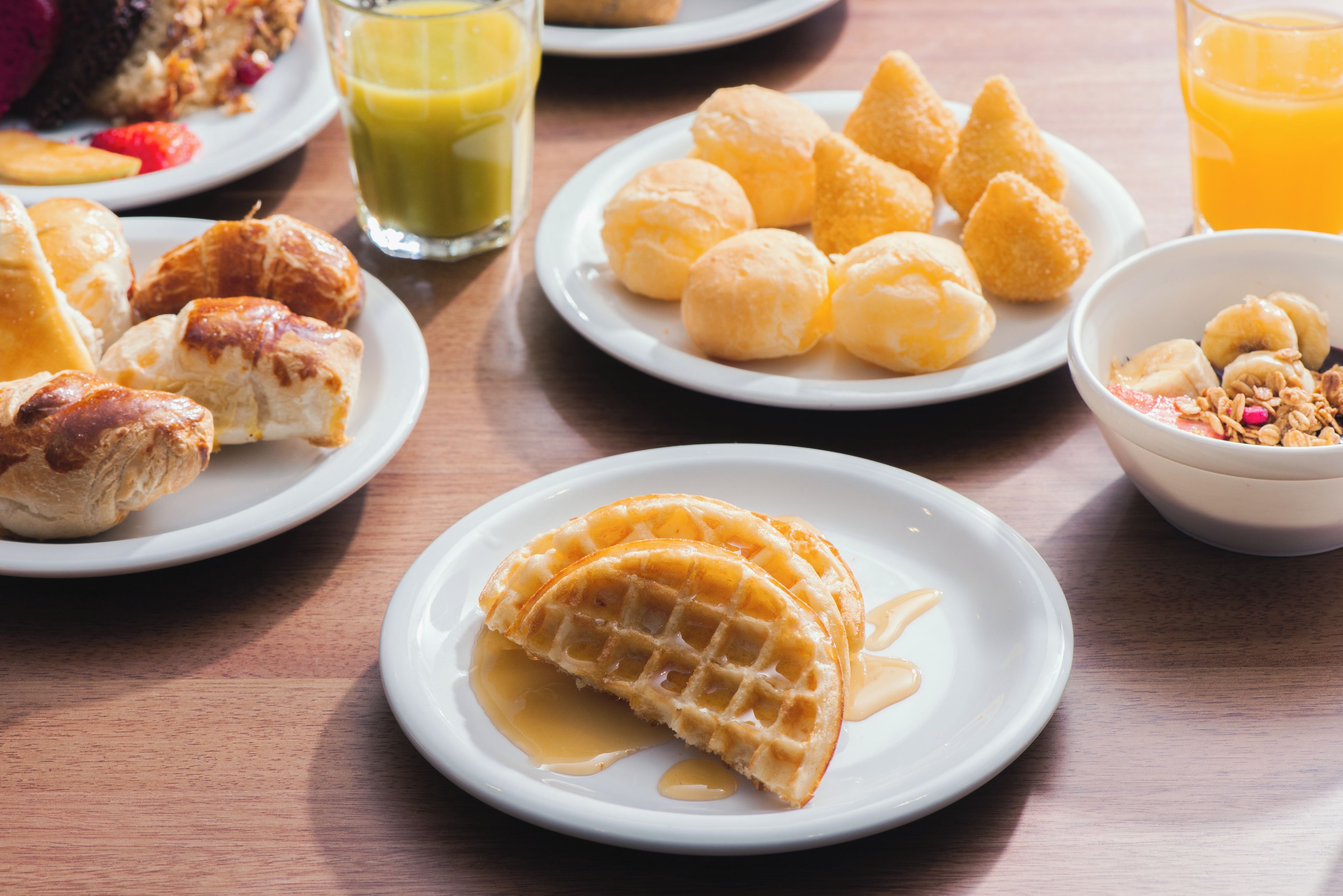 Diversos itens de café da manhã em pratos, incluindo doces, waffles e uma tigela de frutas.