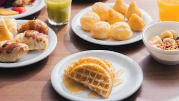 Diversos itens de café da manhã em pratos, incluindo doces, waffles e uma tigela de frutas.