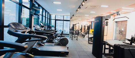 Un gimnasio con cintas de correr, máquinas de pesas y un amplio ventanal que proporciona luz natural.