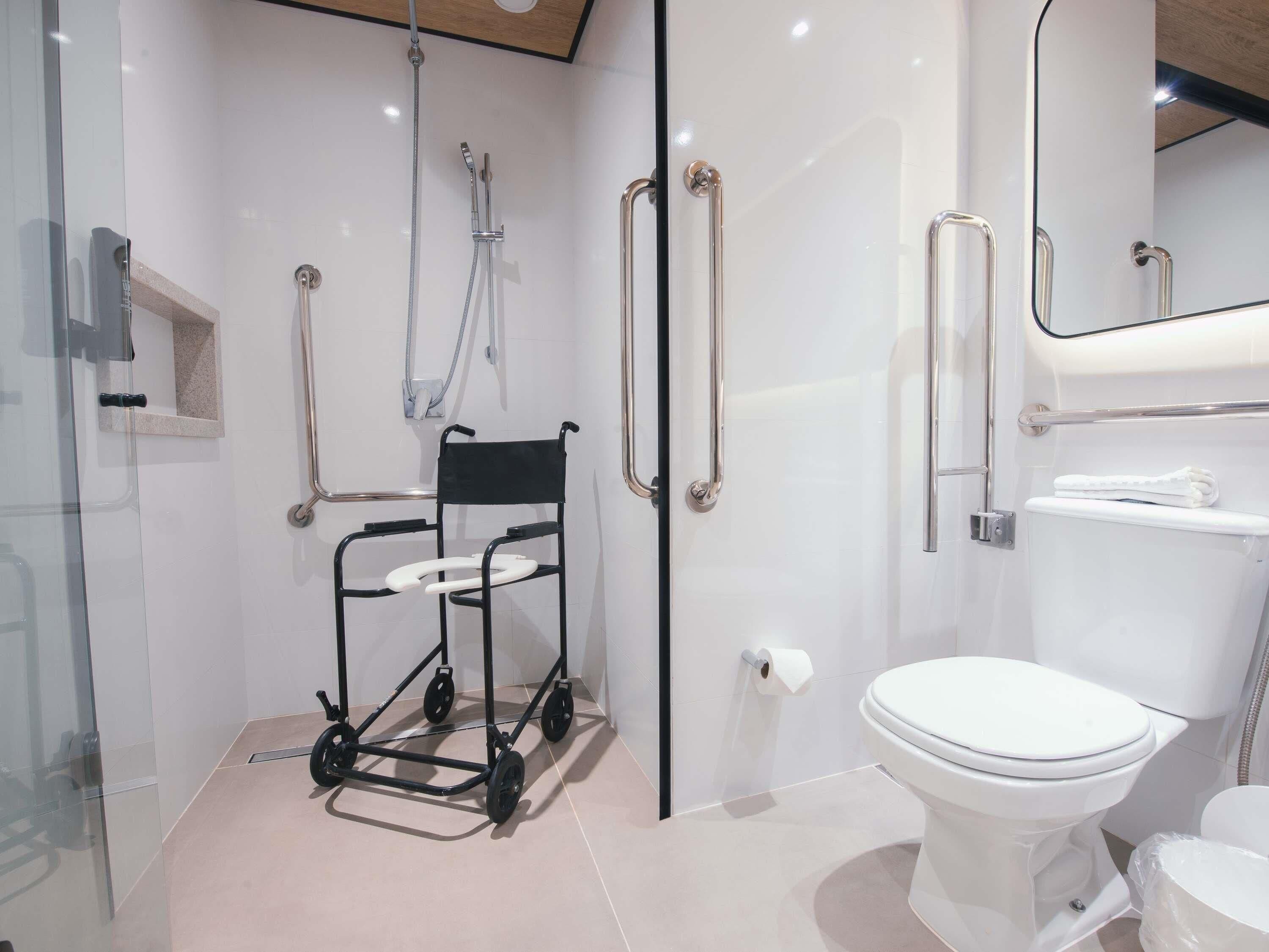 A modern bathroom with a wheelchair-accessible shower, a toilet, and a glass-enclosed shower area.