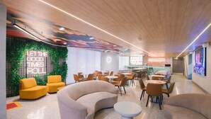 A modern lounge area with seating, a bar, and a green wall with a neon sign. - Ibis Curitiba Shopping (Curitiba)