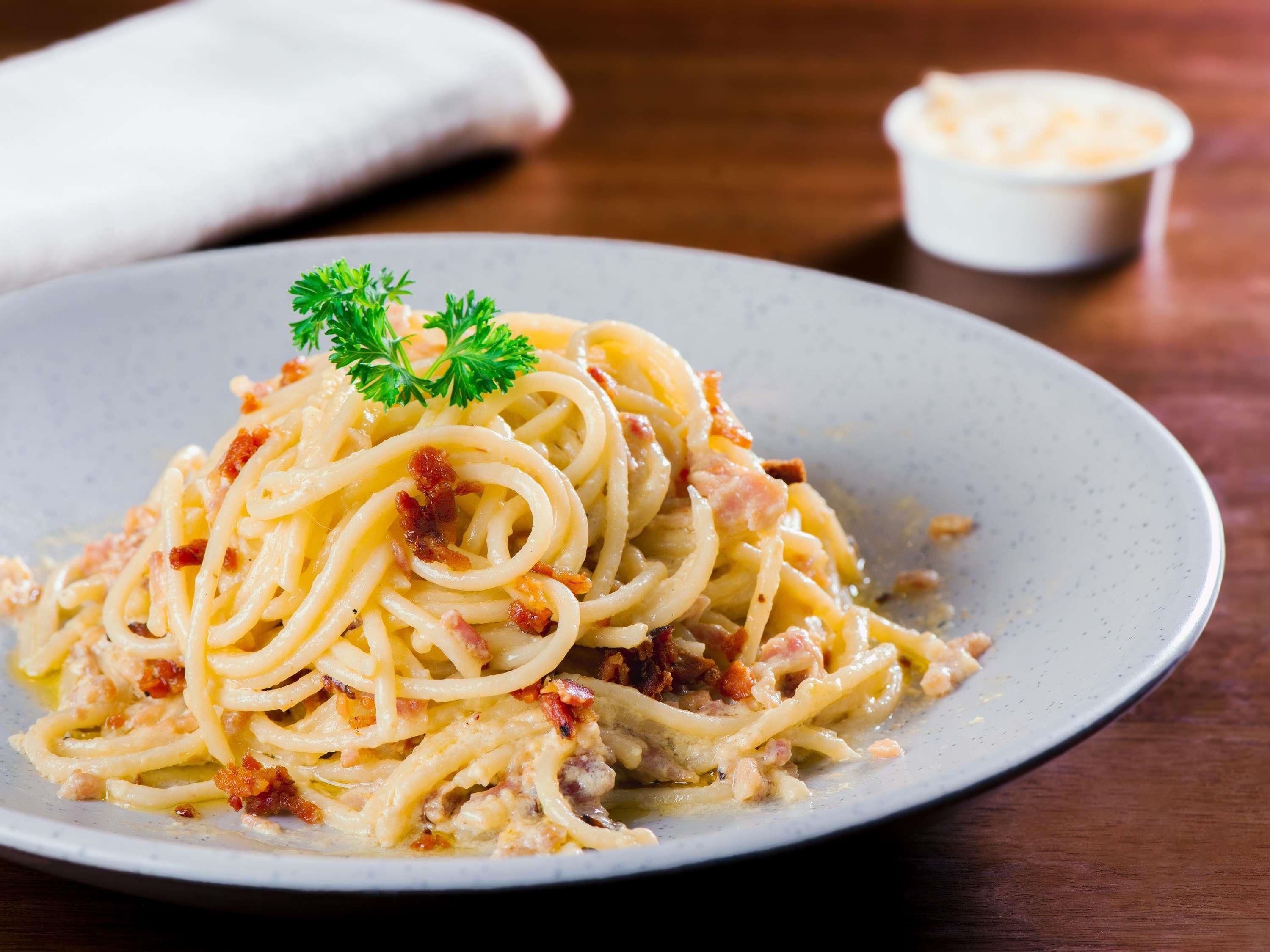 A plate of spaghetti with bacon and a garnish of parsley.