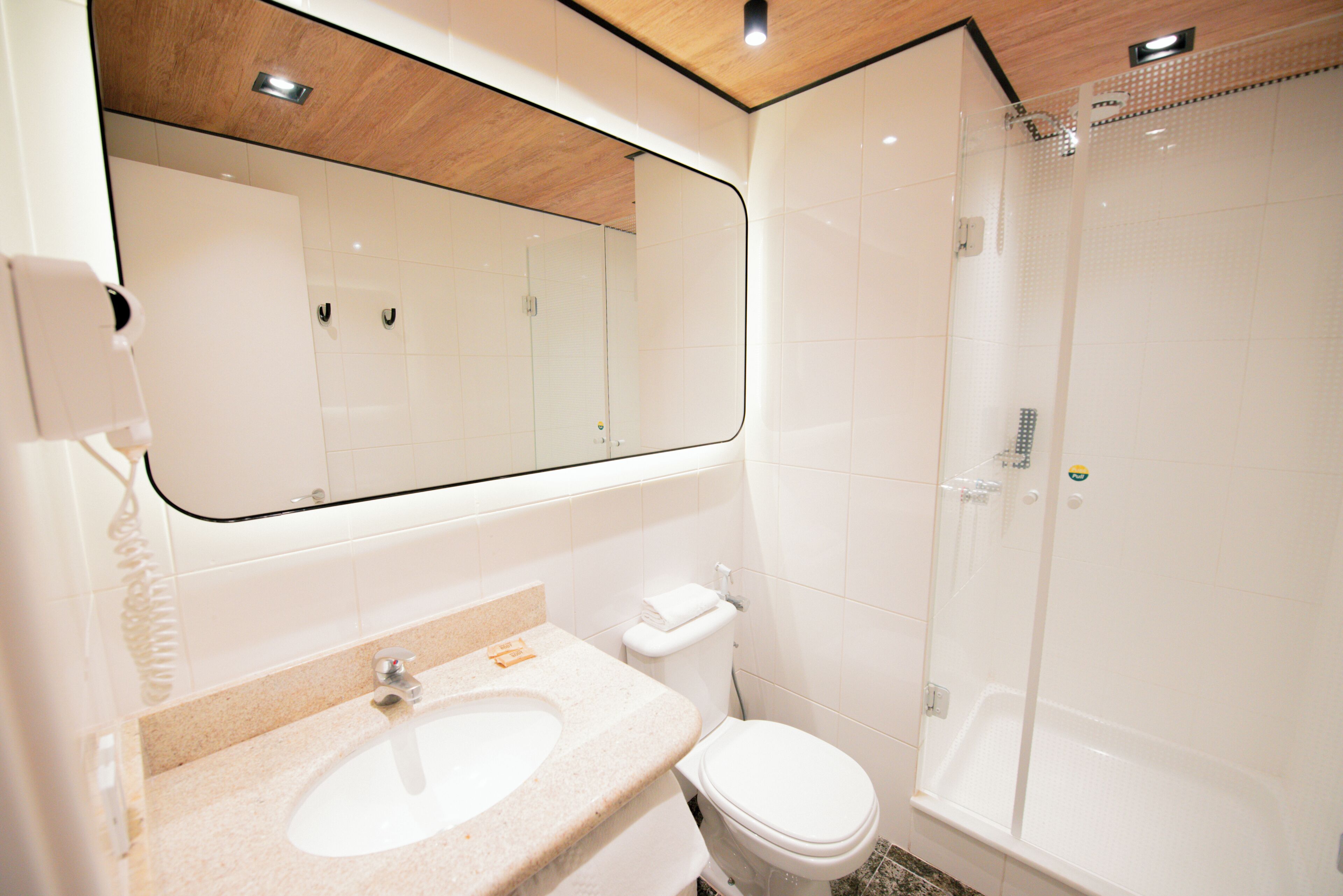 A bathroom with a large mirror, a sink, a toilet, and a shower.